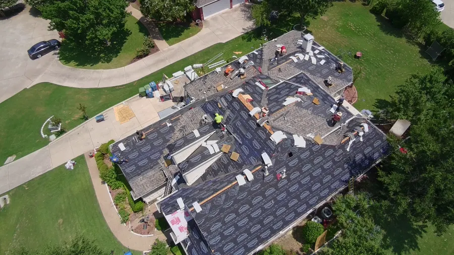 Crew laying underlayment on a large single-story roof, materials staged on the driveway