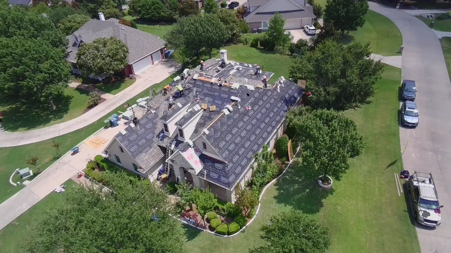 Aerial view of a brick home with the roof dried in and shingle bundles staged along the ridge
