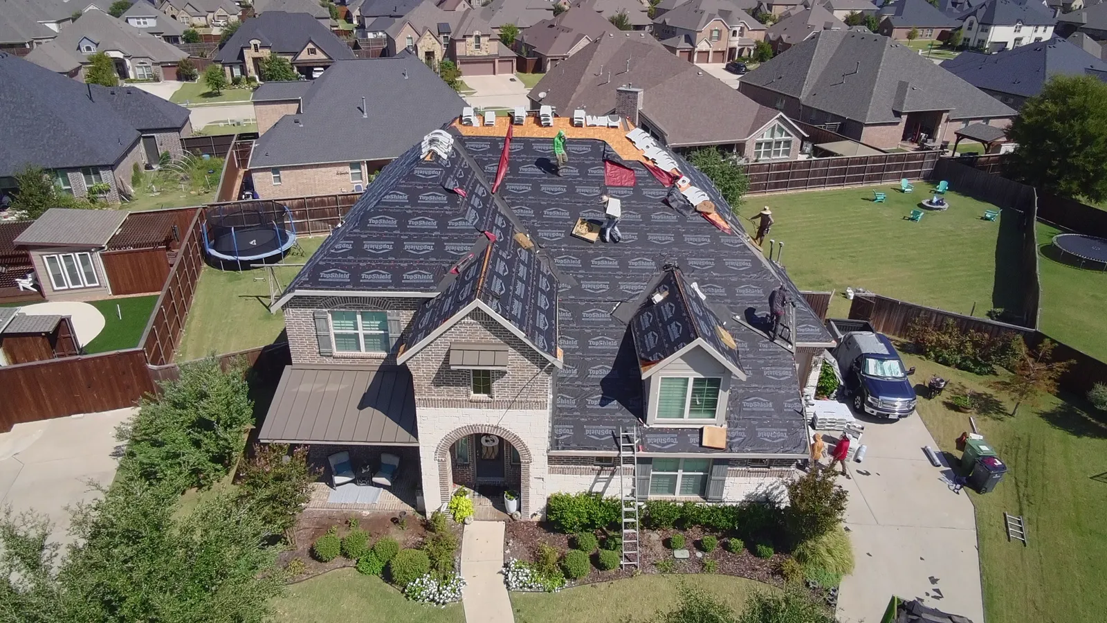 Aerial view of a large two-story brick home with synthetic underlayment going down across the roof