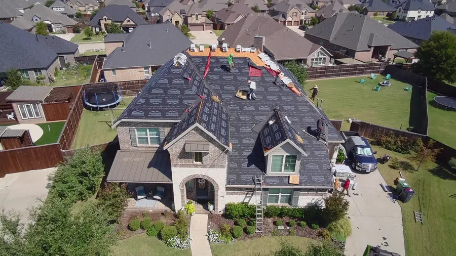 Aerial view of a large two-story brick home with synthetic underlayment going down across the roof