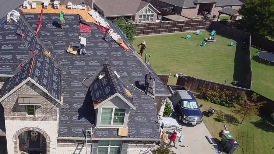 Detail: the crew at the ridge of the same roof, shingle bundles staged on the underlayment