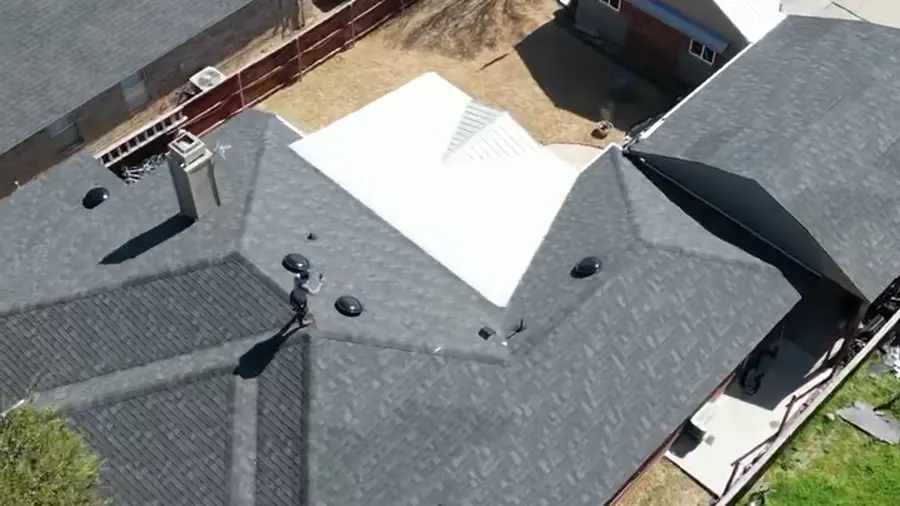 Drone view of a finished dark-shingle roof over a brick single-story home